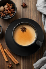 Traditional Indian masala chai tea with milk and spices in a black cup on a dark wooden background