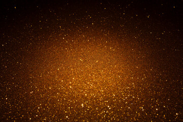 Warm golden surface illuminated in the center reveals dense micro texture, sparkling particles spread outward like glowing embers fading into shadow