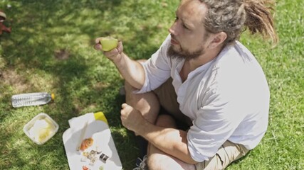 Man with dreadlocks eating apple during picnic lunch