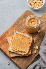 Peanut butter toast on a wooden board on a light background with scattered nuts, napkin and knife.