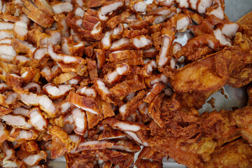 Crispy fried pork belly pieces on metal tray, freshly cooked Thai-style fried pork, commonly sold in local markets or street food stalls. 