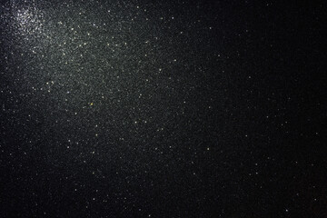 Black glitter texture with asphalt like relief and scattered sparkles, illuminated from upper left corner