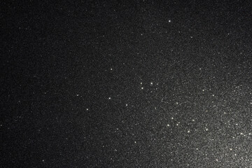 Black glitter texture illuminated from lower right, abstract surface detailed with countless sparkles resembling starlight fading smoothly into dark depth