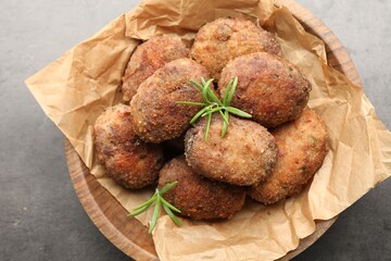 Delicious patties with rosemary in bowl on grey textured table, above view