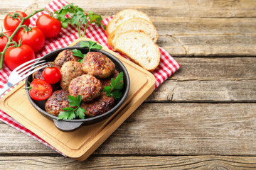 Delicious patties with parsley, tomatoes in pan and fork on wooden table, closeup. Space for text