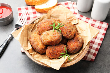 Delicious patties with rosemary in bowl on grey textured table, closeup