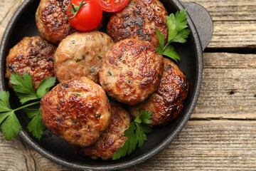 Delicious patties with parsley and tomatoes in pan on wooden table, top view