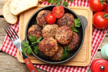 Delicious patties with parsley, tomatoes and bread served on wooden table, flat lay