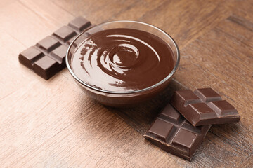 Bowl with melted chocolate and pieces on wooden table, closeup