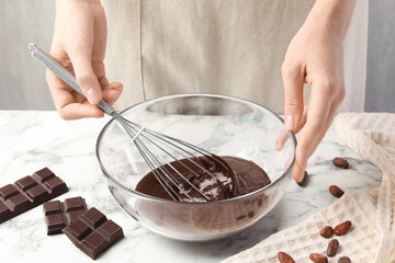 Woman mixing melted chocolate in bowl at white table, closeup