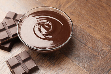 Bowl with melted chocolate and pieces on wooden table, closeup. Space for text