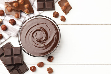 Melted chocolate and pieces with hazelnuts on white wooden table, flat lay. Space for text
