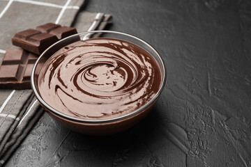Bowl with melted chocolate and pieces on black table, closeup. Space for text