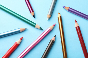 Colorful eye pencils on light blue background, flat lay