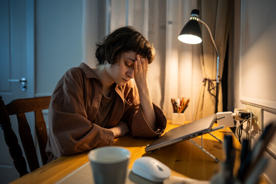 Weary female rests head in palms after laptop work of late hour. Tired young woman fatigue, sleep deprivation, mental exhaustion, emotional burnout, deadline pressure, depressed woman burnout
