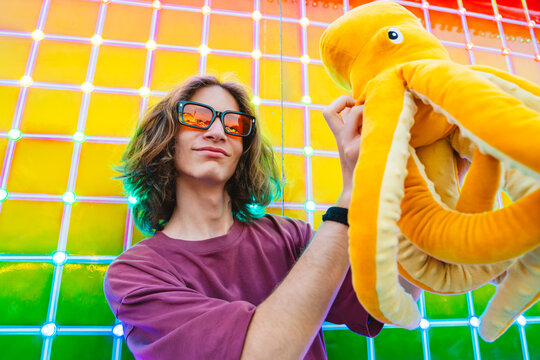 Teenager enjoying neon-lit amusement park holding plush octopus at night