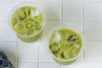 From Top View,Two cups of iced matcha latte on white ceramic table. Refreshing green drink for cafe menu, summer beverage, or healthy lifestyle theme.
