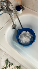 Handwashing clothes in bucket under bathtub faucet