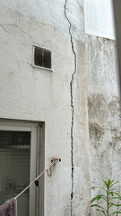 Large vertical crack on exterior plaster wall by window