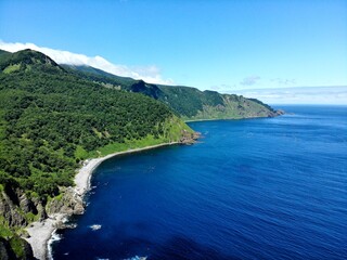 Curving pebble beach and green sea cliffs along deep-blue bays of the Shiretoko Peninsula, Hokkaido, Japan &mdash; aerial summer view of the Sea of Okhotsk