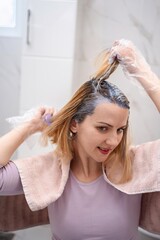 Fototapeta premium Woman dyeing her hair at home in the bathroom