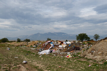 Against a mountainous backdrop, waste and plastic trash piled up in an open area. Environmental pollution and nature.