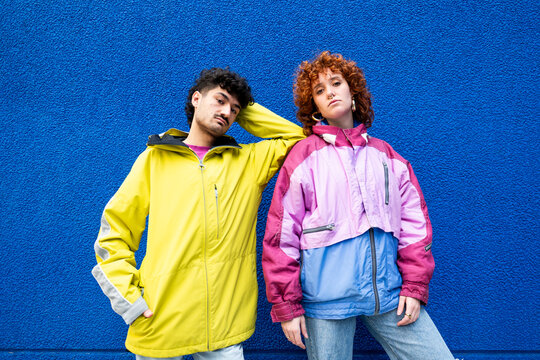 Two friends in colorful urban clothing posing against a blue background