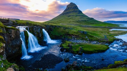 Breathtaking view of Kirkjufell mountain and its cascading waterfalls during a vibrant sunset in Iceland. The serene atmosphere enhances the awe-inspiring natural beauty of the landscape.