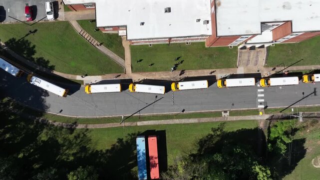 Aerial top down shot showing row of traditional american school buses in row. Sunny in american school area. Summer season with cars on parking area