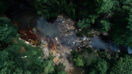 Obraz premium Aerial view of a forest stream winding through rocky terrain with steam and colorful mineral deposits. Concept Aerial Forest Stream, Winding Rocky Terrain, Steam Rising, Colorful Mineral Deposits