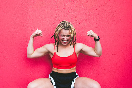 Athlete with dreadlocks flexing muscles in red activewear against wall