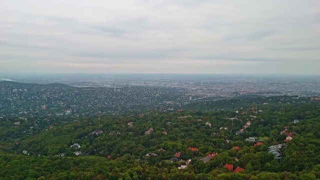 Aerial hyperlapse from the forested landscape around Normafa with Budapest cityscape in the background on an overcast day in Hungary.