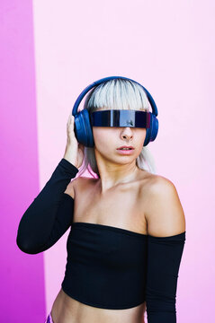 Futuristic woman with visor glasses and headphones on pink background