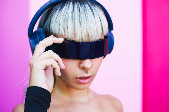 Futuristic woman with headphones and visor glasses in pink setting