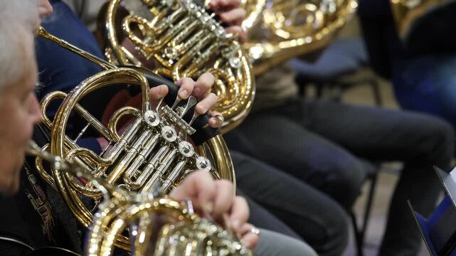 Musicians playing French horns in close-up of hands and instruments