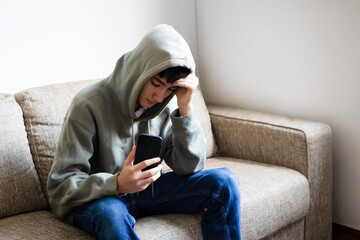 Cyberbullying, negative in social media online issue in teenager. Upset teen boy sitting near...