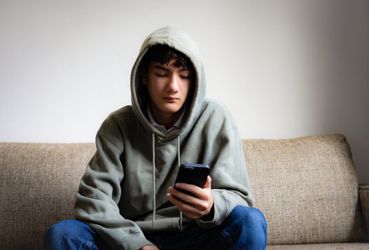 Cyberbullying, negative in social media online issue in teenager. Upset teen boy sitting near window using smartphone at home. 
