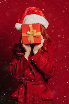 Person in Santa hat holding Christmas gift box on red background