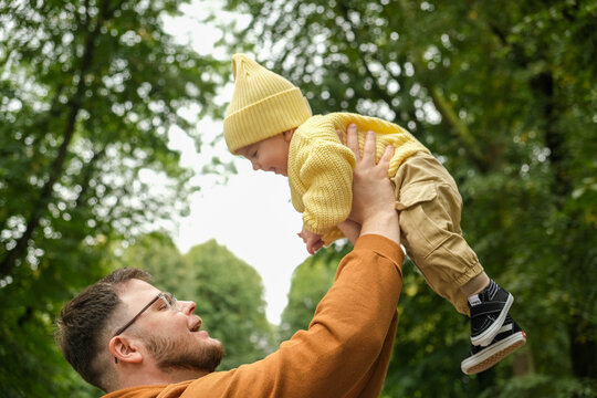 Father Lifting Baby in Park Early Autumn - Powered by Adobe