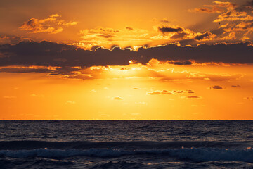 Beautiful sunrise over the sea horizon with scenic clouds and sun rays