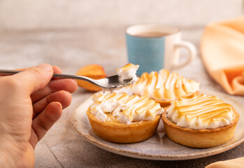 French lemon tart with meringue with hand on brown concrete, orange linen textile, side view, close up, selective focus