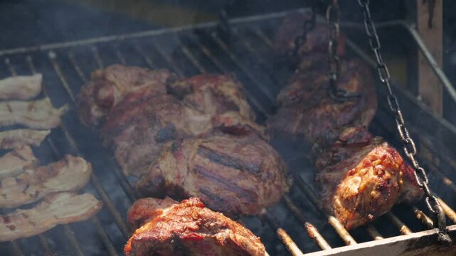 Close-up of grilling meat on an outdoor barbecue grill in summer. Preparing beef and chicken over smoky charcoal. Picnic time with an outdoor grill party. High quality 4k footage
