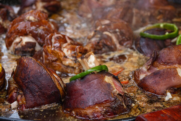 Baked pork knuckle with vegetables in a large frying pan close-up. Cooking shank outdoors at a food festival. It is often cooked with beer, garlic, mustard, and other spices.