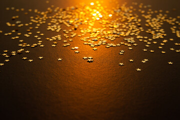 Étoiles dorées scintillantes sur un fond brun, étoiles en haut de l'image, rayon de lumière dorée centré sur l'image, ambiance de Noël et de fêtes de fin d'année