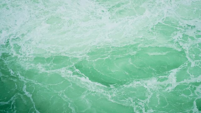 Foamy waves swirling in turquoise sea behind moving ferry. Churning water pattern forming vibrant texture from ship wake. Ocean surface bubbling with white trails after passing vessel