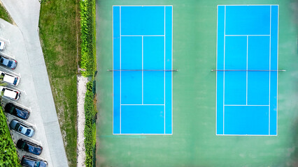 Blue tennis courts from above, showing nets and white lines, surrounded by green landscaping and an...