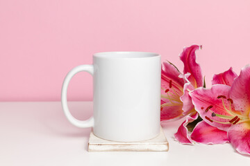 White mockup mug with pink lily flower on pink background. Coffee or tea mockup cup for festive design, wedding, valentine, birthday, mother day or woman day holiday