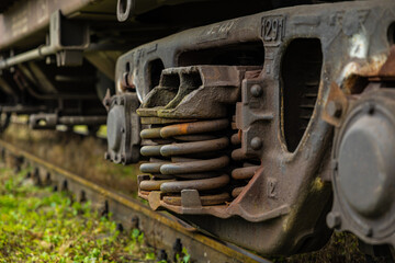 Close-up of rust-covered train suspension coil springs within an aged bogie frame, showing detailed texture, corrosion, and industrial wear on the railway track