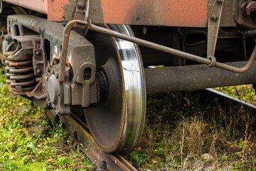 Close-up of a polished steel train wheel on a weathered freight bogie with visible springs and aged metal components, resting on grassy railway tracks