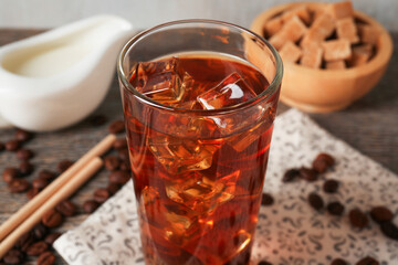 Tasty coffee with ice in glass, beans, milk and sugar cubes on wooden table, closeup